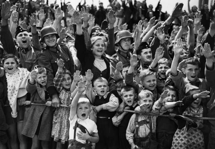 Толпа женщин, детей и солдат с фирменным приветственным знаком нацистов. Франция